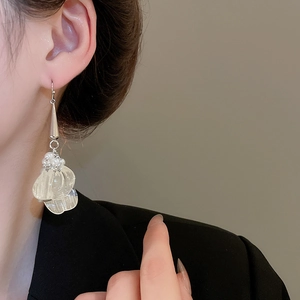 Close-up of hollow petal pearl fringe drop earrings worn on a model with black suit