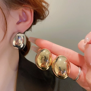 Detail of gold and silver bean-shaped earrings featuring a polished metallic finish