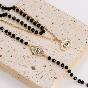 Gold evil eye necklace with black glass beads on natural stone background