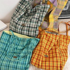 Detailed pile of colorful checkered canvas tote bags showing fabric texture and metal logo