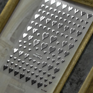 Detail of 3D silver heart nail stickers on a vintage gold frame for luxury nail art