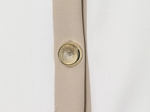 Macro detail of white fabric with khaki trim and a textured golden button on a blazer