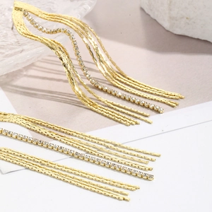 Macro view of long gold tassel earrings with rhinestone chain and snake bone links