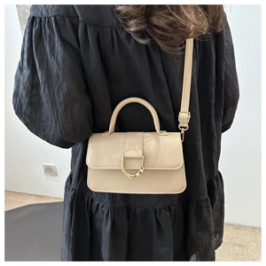 Detail of a beige leather crossbody bag with a gold D-ring buckle on a model