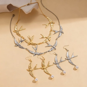 Detailansicht der Schwalben-Halskette und passender Perlenohrringe in Gold und Silber