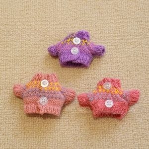 Close-up of hand-knitted mini doll sweaters with white buttons and jacquard patterns