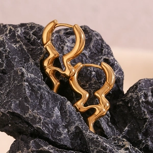 Macro view of gold-plated liquid earrings on black stone with smooth metallic finish
