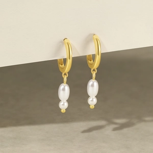 Detail of gold hoop earrings featuring vertical white double pearl pendants and a polished finish