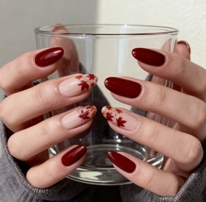 Detail of almond-shaped autumn nails with maple leaf art and deep red glossy finish