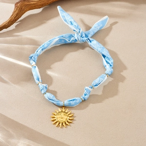 Detail of light blue paisley ribbon choker with a golden sun face charm on sand background