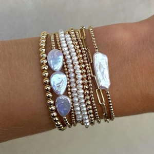 Close-up of layered baroque freshwater pearl bracelets and 18K gold beaded chain on wrist