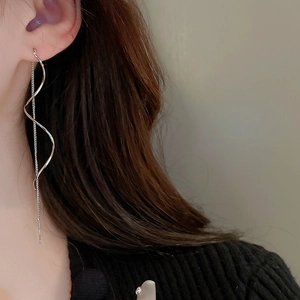 Macro view of silver geometric wave earrings with drop chain tassels on a model