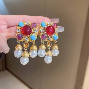 Close-up of vintage gold earrings with red blue purple stones and pearl pendants