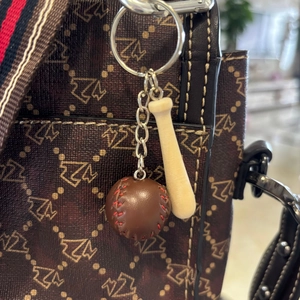 Detailed close-up of mini wooden baseball bat and leather ball keychain on a brown handbag