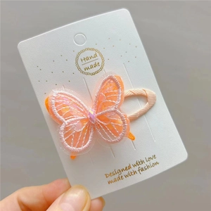 Macro detail of handmade embroidered butterfly hair clip with pink sequins on white card