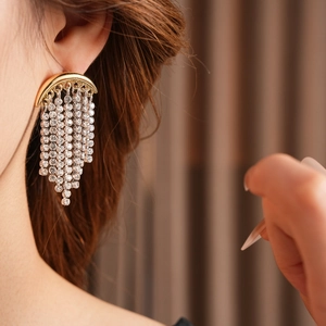 Close-up of elegant gold tassel earrings with shimmering rhinestones worn by a model