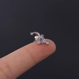 Macro detail of tiny silver crescent and wing cartilage stud with purple zircon on fingertip