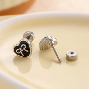 Elegant heart-shaped black studs with silver bows and screw backs on a ceramic plate