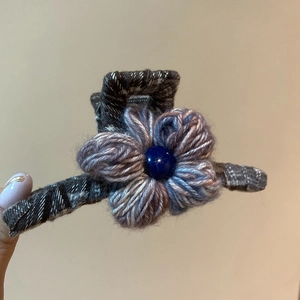 Detail of grey plaid fabric hair claw clip featuring a knitted flower with blue bead