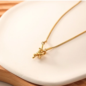 Macro shot of gold knot pendant on a delicate snake chain over white ceramic