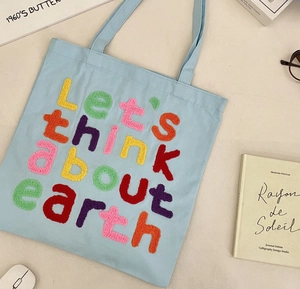 Detail of colorful towel embroidery and 'Let's think about earth' text on blue canvas tote