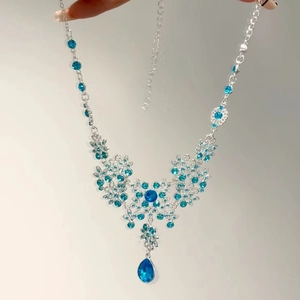 Dettaglio macro della collana argentata con fiori di strass blu e ciondolo a goccia