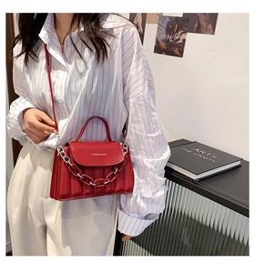 Red leather crossbody bag with chain strap styled on a model in a minimal chic setting