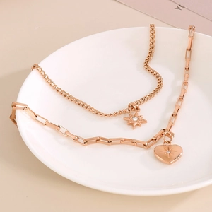 Double-layered rose gold necklace with star and heart pendants on a ceramic plate