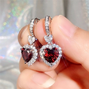 Close-up of a silver heart-shaped earring with a red gemstone and diamond halo inlay