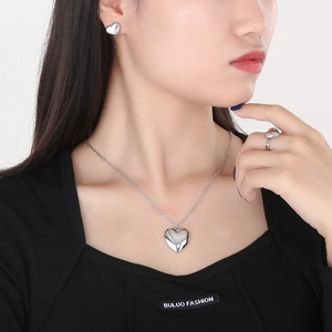 Detailed view of silver heart pendant necklace, stud earrings and ring set on model