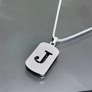 Vue détaillée du pendentif lettre J ajouré en argent sur une chaîne en acier titane