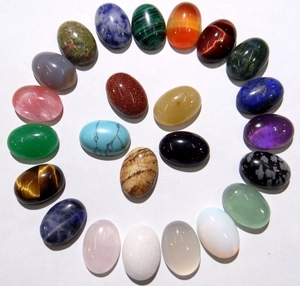 Macro shot of 23 oval gemstone cabochons including tiger eye and turquoise on white backdrop