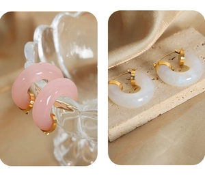 Detail of C-shaped resin earrings in pink and pearl white with golden metal fasteners