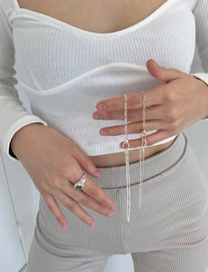 Detail view of a chunky silver ring and layered chains worn with a white knit vest