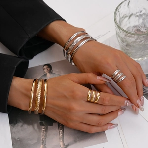 Detail of gold and silver layered cuff bracelet and ring set with a glossy textured finish