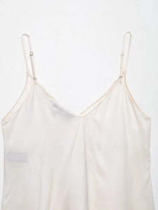 Detail eines elfenbeinfarbenen Satin-Tops mit V-Ausschnitt und verstellbaren Metallschnallen