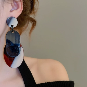 Détail de boucles d'oreilles géométriques en acrylique marbré portées avec un style moderne