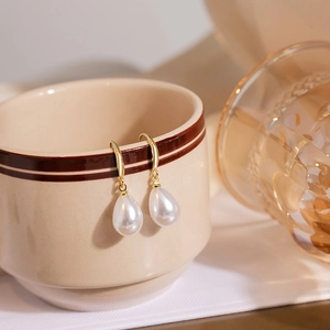 Elegant gold teardrop pearl earrings hanging on a ceramic cup in a lifestyle setting