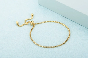 Detail of adjustable gold-plated box chain bracelet with slider clasp and round beads
