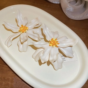 Macro view of white acrylic flower earrings with yellow beaded core on a tray