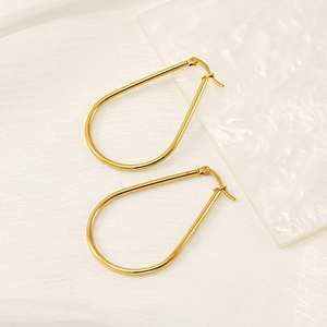 Polished gold teardrop hoop earrings in minimalist style on a white textured background