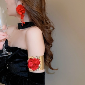 Detail of red fabric flower earrings with tassels and matching gold floral arm cuff jewelry