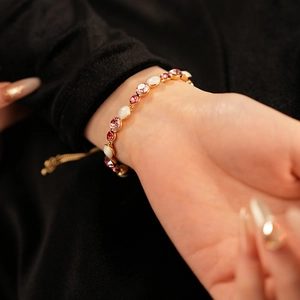 Détail d'un bracelet doré ajustable avec pierres roses et blanches porté au poignet