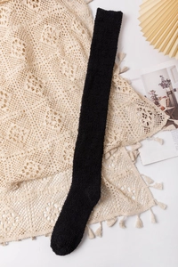Detail view of thick black coral fleece over-the-knee socks on a cozy lace background