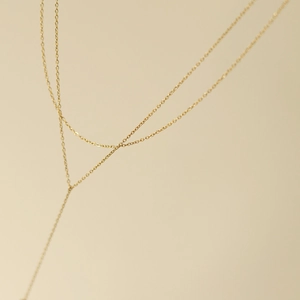Detailed macro view of minimalist double-layered Y-shaped gold chain with tassel detail