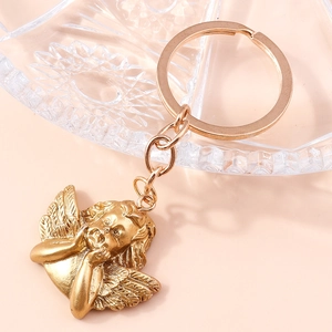 Close-up of golden angel keychain charm with detailed wing texture on a glass tray