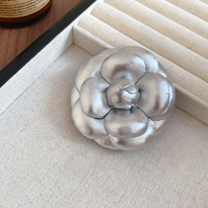 Detailed close-up of a silver camellia flower brooch on a soft cream jewelry tray