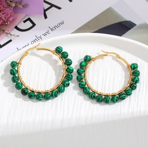 Detail of handmade gold wire-wrapped hoop earrings with malachite beads on a white tray