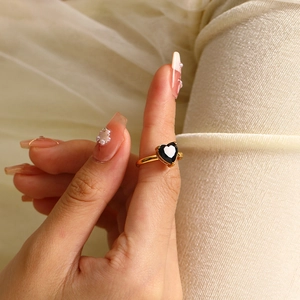 Macro shot of an elegant gold heart ring featuring a black gemstone on model's finger