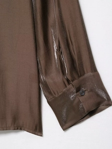 Close-up of a dark brown satin shirt cuff with a black button and smooth silk texture